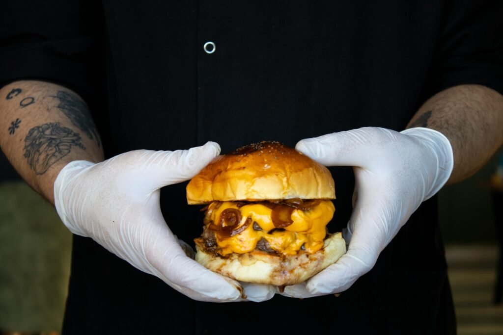 El sin gluten también se mueve por la calle A mouthwatering cheeseburger held by gloved hands, showcasing melty cheese and juicy beef patty.